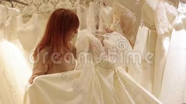店员帮助年轻漂亮的女士在婚纱店挑选婚纱